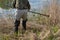 Man with rubber boots scything overground rushes by the lake shore. Man cutting bulrushes with old scythe outside on a sunny day