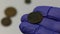 A man in rubber gloves examines antique copper coins covered in corrosion. Prepares for their cleaning and patina