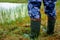 A man in rubber wool boots stands moss at the edge of the lake.