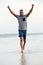 Man running barefoot on beach with arms raised in victory