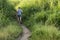 A man runs uphill through a dirt trail surrounding by tall grasses. Jogging outdoors. Active lifestyle