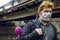 Man in rustic mask on face with bag and hipster pink toy behind in decay outdoor environment