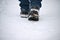 A man\\\'s feet in winter warm, comfortable shoes take a step on a snowy road in the park on a winter walk.