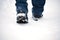 A man\'s feet in winter warm, comfortable shoes take a step on a snowy road in the park on a winter walk.