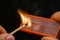 Man\'s fingers lighting a match, setting fire on friction. On a black background. Matches and fire. Smoke