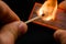 Man\'s fingers lighting a match, setting fire on friction. On a black background. Matches and fire. Smoke