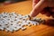 A man\\\'s hand assembles a puzzle on a table.