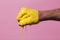 Man`s hand clenched into a fist smeared in yellow paint on a pink color studio background, a creative idea advertising dye,