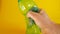 A man`s hand crushes a green disposable plastic bottle on a yellow background, footage ideal for topics like ecology and