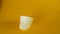 A man`s hand crushes a white disposable plastic cup on a yellow background, footage ideal for topics such as ecology and