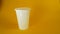 A man`s hand crushes a white disposable plastic cup on a yellow background, footage ideal for topics such as ecology and