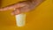 A man`s hand crushes a white disposable plastic cup on a yellow background, footage ideal for topics such as ecology and