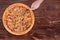 Man`s hand cuts the pizza with chicken breast, corn, bacon and mushrooms, with a pizza cutter on round wood plate