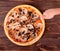 Man`s hand cuts the pizza with ham, mozzarella, mushrooms and olives, with a pizza cutter on round wood platter which is on wood