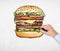 A man\'s hand is drawing a colourful burger. A concept of fast food.