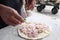 Man`s hand dressing an uncooked onions pizza on a marble table with copy space for your text
