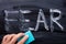 Man`s Hand Erasing Fear Word With Blue Sponge