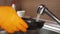 A man's hand in a glove with a sponge washes a dirty frying pan. Wash the pan with a sponge and detergent
