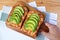 Man`s hand holding a breadboard of grilled cheese toast with tomato and sliced avocado