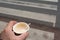 Man`s hand holding a disposable paper cup with hot coffee as walking on zebra crossing in the city