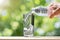 Man`s hand holding drinking water bottle water and pouring water into glass on wooden tabletop on blurred green bokeh background w