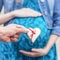 Man`s hand holding gingerbread heart with red ribbon on the pregnant belly background. Parenthood and love concept. Instant squar