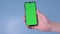 Man`s hand holding a mobile telephone with a vertical green screen chroma key smartphone technology cell phone on blue.