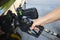 Man`s hand holding nozzle of gas pump and putting gas into black car