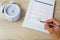 Man`s hand holding pen and marking on calendar on blurred blue classic alarm clock on vintage wooden table