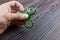 A man's hand holding and playing metal green color fidget spinner with wooden table background