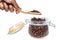 A man`s hand holding wooden spoon to scooping roasted coffee beans from glass jar in white background