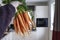 Man`s hand holds a bunch of fresh, raw carrots tied with a string on a blurred background of a cozy kitchen