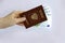 A man s hand holds a foreign passport of the Russian Federation with banknotes of 100 euros inside on a light background. Travels