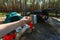 The man\'s hand holds an iron mug with a warm drink on the background of the table and chairs, campfire, a tent and an SUV in camp