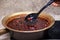 A man& x27;s hand holds a large spoon with strawberry jam on the background of Strawberry jam cooked in a copper basin.