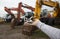 man\'s hand holds small toy excavator in his palm. Behind him, out of focus, a row of real excavators with large buckets