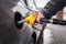 A man`s hand holds a yellow refueling gun inserted into the opening of the car`s gas tank when refueling with gasoline. Close-up