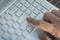 Man`s hand on notebook keyboard on a light background guy presses the enter button on the gray keyboard of modern