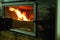 A man`s hand opens the glass door of the fireplace in which the wood is burning. Modern closed fireplace with glass