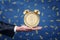 Man`s hand with palm facing up to hold an alarm clock with a stylized dollar coin instead of clock face on blue