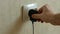 A man`s hand plugs a charger into a faulty socket. An electrical outlet sticks out of the wall in the apartment. Problems with ele