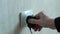 A man`s hand plugs a charger into a faulty socket. An electrical outlet sticks out of the wall in the apartment. Problems with ele