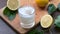 Man`s hand pours lemon juice from pitcher into glass with ice on wooden board. Close up.