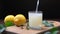 Man`s hand pours lemon juice from pitcher into glass on wooden board. Close up.