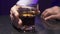 Man`s hand puts glass of alcohol liquid with ice on surface of black table