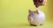 Man`s hand putting coins in piggy bank of pig shape on yellow background.