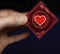 Man\'s hand with a red condom pack and heart symbol on it