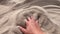 Man\'s hand scatters sand through his fingers.