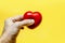 Man`s hand squeezes a red toy heart on a yellow background