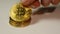 A man's hand stacks gold Bitcoin cryptocurrency coins in a column on a white background.